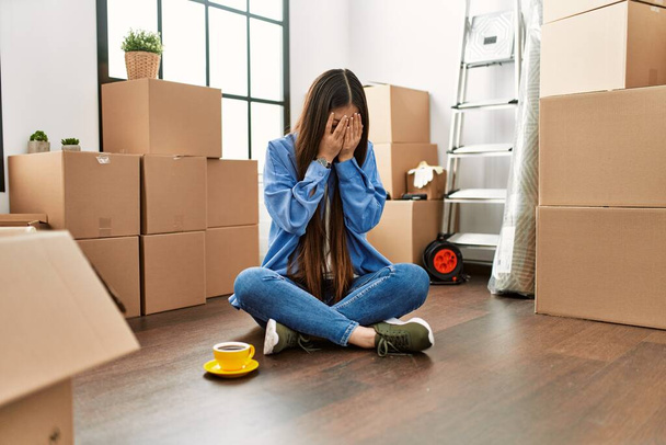 Giovane ragazza cinese seduta sul pavimento nella nuova casa con espressione triste che copre il viso con le mani mentre piange. concetto di depressione.  - Foto, immagini