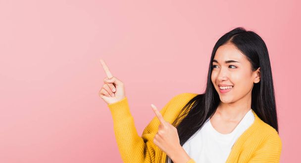 Asian happy portrait beautiful cute young woman standing makes gesture two fingers point upwards above presenting product something, studio shot isolated on pink background with copy space - Fotó, kép