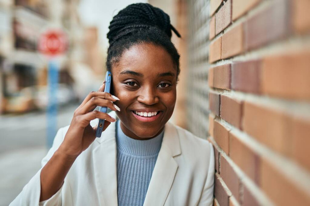 Junge afrikanisch-amerikanische Geschäftsfrau lächelt fröhlich auf dem Smartphone in der Stadt. - Foto, Bild