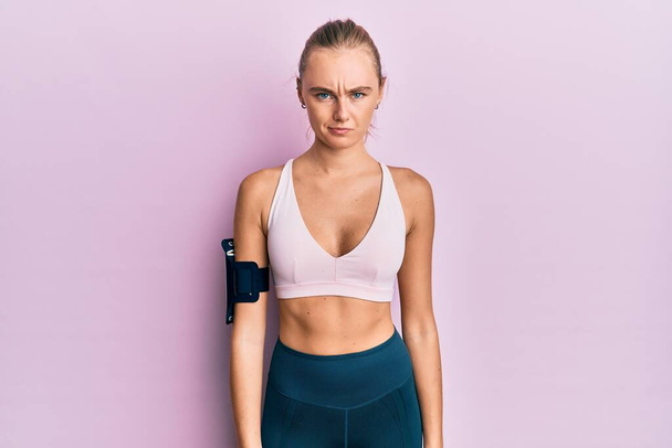 Beautiful blonde woman wearing sportswear and arm band skeptic and nervous, frowning upset because of problem. negative person.  - Foto, immagini