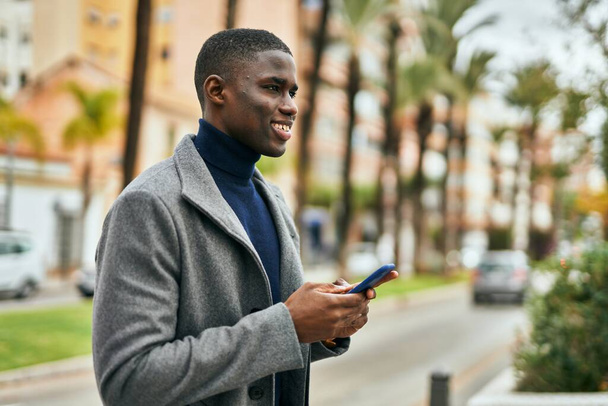 Nuori afrikkalainen amerikkalainen mies hymyilee onnellisena älypuhelimella kaupungissa - Valokuva, kuva