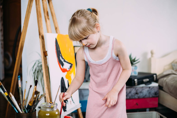 小さなかわいい女の子は大きな絵を描いていますアクリルで自宅でAイーゼル.  - 写真・画像