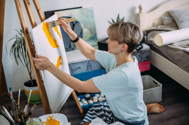 Νεαρή γυναίκα καλλιτέχνης ζωγραφίζει στο σπίτι σε ένα δημιουργικό σκηνικό στούντιο. - Φωτογραφία, εικόνα