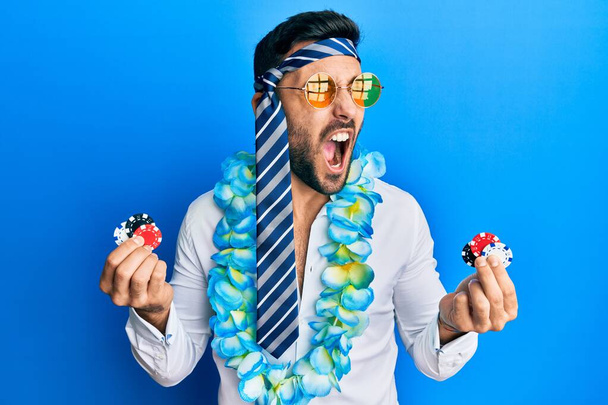 Young hispanic businessman wearing party funny style holding casino chips angry and mad screaming frustrated and furious, shouting with anger. rage and aggressive concept.  - Foto, immagini