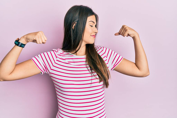 Young brunette woman wearing casual clothes over pink background showing arms muscles smiling proud. fitness concept.  - Фото, изображение