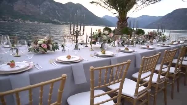 Egy asztal egy esküvői lakomán, virágokkal, gyertyatartókkal és fiatal gránátalmákkal díszítve a Kotori-öböl mólóján. - Felvétel, videó