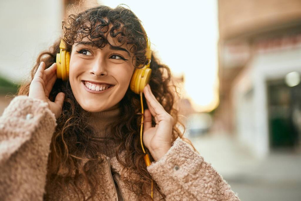 Joven mujer hispana sonriendo feliz usando auriculares en la ciudad - Foto, imagen