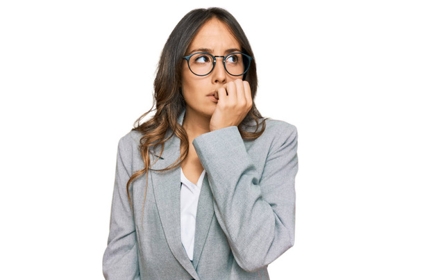Jonge brunette vrouw draagt zakelijke kleren die er gestrest en nerveus uitzien met handen op de mond bijtende nagels. angstprobleem.  - Foto, afbeelding