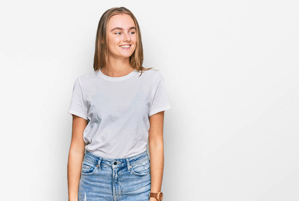 Beautiful young blonde woman wearing casual white t shirt looking away to side with smile on face, natural expression. laughing confident.  - Photo, Image