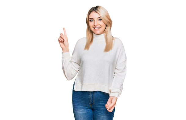 Mulher caucasiana jovem vestindo camisola de inverno casual com um grande sorriso no rosto, apontando com o dedo da mão para o lado olhando para a câmera.  - Foto, Imagem