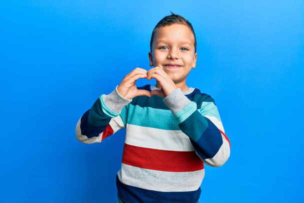 Little kid boy wearing striped sweater smiling in love doing heart symbol shape with hands. romantic concept.  - Фото, изображение