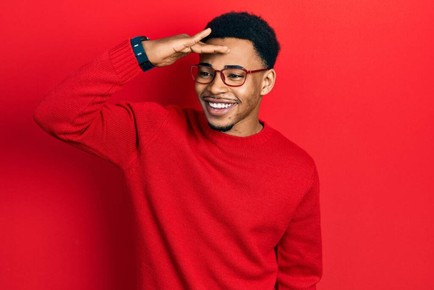 Young african american man wearing casual clothes and glasses very happy and smiling looking far away with hand over head. searching concept.  - Φωτογραφία, εικόνα