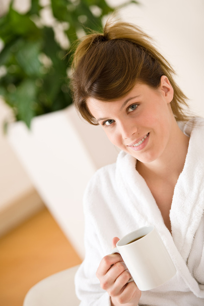 Young woman in white bathrobe with coffee in lounge - Zdjęcie, obraz