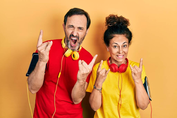 中年カップルのヒスパニック系女性と男性が両手を上げて岩のシンボルをやって狂気の表現で叫んでスポーツウェアと腕バンドを身に着けています。音楽スター。重い概念は.  - 写真・画像