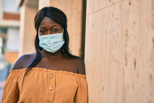 Tıbbi maske takan genç Afro-Amerikan kadın şehirde dikiliyor.. - Fotoğraf, Görsel