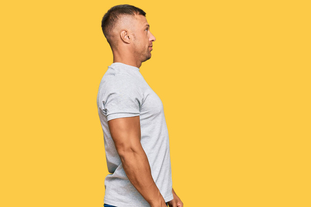 Hombre musculoso guapo con camiseta gris casual mirando hacia un lado, pose de perfil relajado con cara natural con sonrisa confiada.  - Foto, Imagen