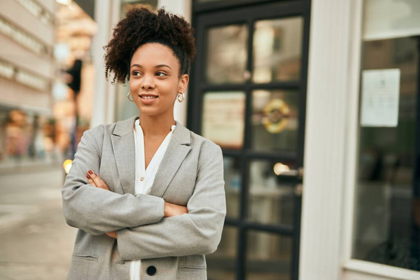 Νεαρή αφροαμερικανή επιχειρηματίας με σταυρωμένα χέρια στέκεται στην πόλη. - Φωτογραφία, εικόνα