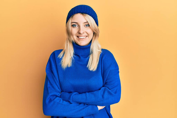 Young caucasian woman wearing wool winter sweater and cap happy face smiling with crossed arms looking at the camera. positive person.  - Foto, imagen