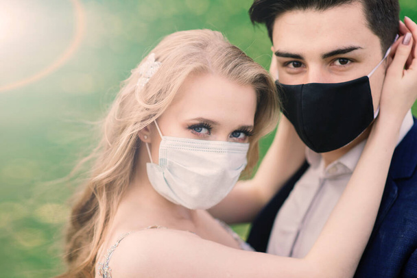 Jonge liefdevolle paren lopen in medische maskers in het park tijdens quarantaine op hun trouwdag. Coronavirus, ziekte, bescherming, ziek. Europese viering geannuleerd. - Foto, afbeelding
