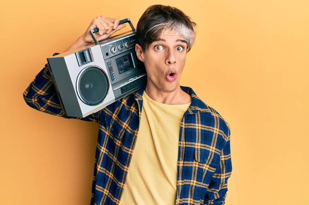 Young hispanic man holding boombox, listening to music scared and amazed with open mouth for surprise, disbelief face  - Photo, Image