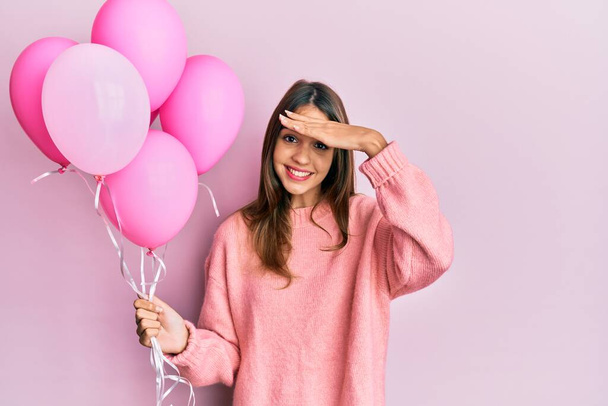 Молода брюнетка жінка тримає рожеві кульки напруженими і розчарованими руками на голові, здивованим і розлюченим обличчям
  - Фото, зображення