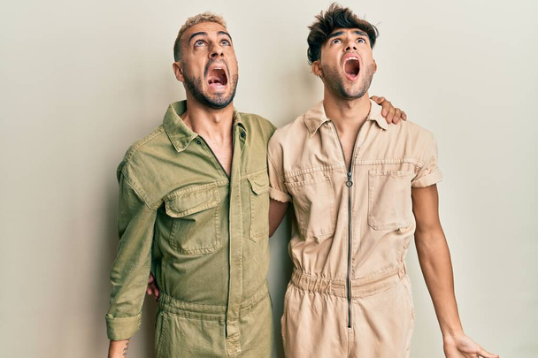 Ομοφυλόφιλο γκέι ζευγάρι που στέκεται μαζί φορώντας casual φόρμα θυμωμένος και τρελός ουρλιάζοντας απογοητευμένοι και έξαλλος, φωνάζοντας με θυμό. οργή και επιθετική αντίληψη.  - Φωτογραφία, εικόνα