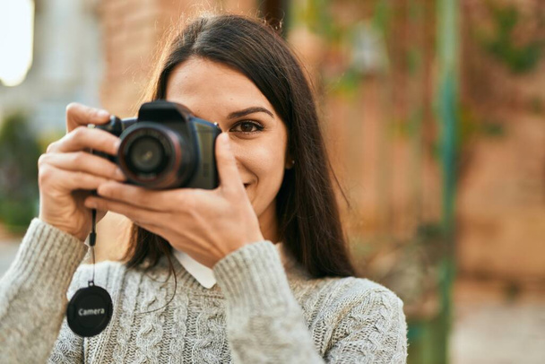 Giovane donna ispanica sorridente felice utilizzando la fotocamera in città. - Foto, immagini