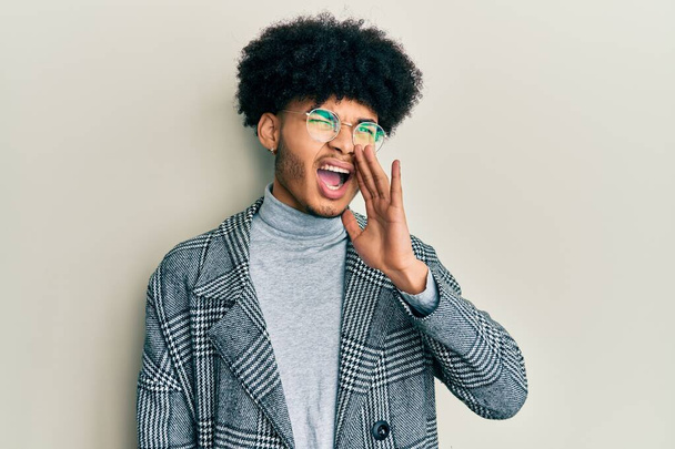 Young african american man with afro hair wearing casual clothes  glasses shouting and screaming loud to side with hand on mouth. communication concept.  - Valokuva, kuva