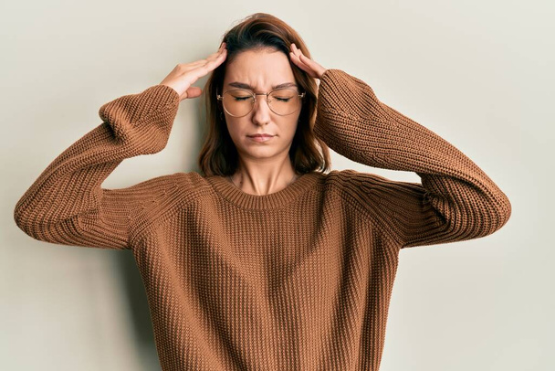 Jonge blanke vrouw draagt casual kleding en een bril met de hand op het hoofd, hoofdpijn omdat stress. lijden aan migraine.  - Foto, afbeelding
