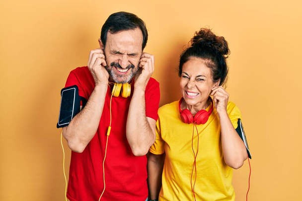Paar mittleren Alters, hispanische Frau und Mann in Sportkleidung und Armreif, die die Ohren mit Fingern bedecken, die genervt sind von dem Lärm lauter Musik. Gehörloses Konzept.  - Foto, Bild