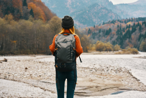 mujer viaja en las montañas en otoño cerca del río en la naturaleza con una mochila vista trasera - Foto, Imagen