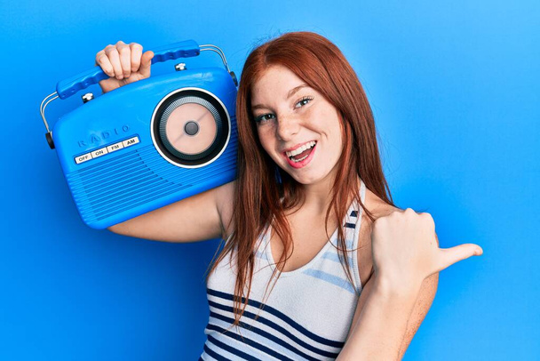 Nuori punainen pää tyttö tilalla vintage radio osoittaa peukalo ylös puolelle hymyillen onnellinen suu auki  - Valokuva, kuva