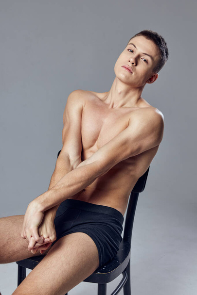 handsome male athlete in black shorts sitting on a chair posing - Foto, afbeelding
