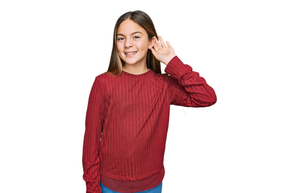 Beautiful brunette little girl wearing casual sweater smiling with hand over ear listening an hearing to rumor or gossip. deafness concept.  - Фото, зображення