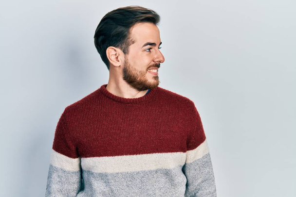 ハンサムなcaucasian男で髭を生やしてカジュアル冬のセーターを身に着けています横に見て、自然な顔と自信を持って笑顔でプロファイルのポーズをリラックス.  - 写真・画像