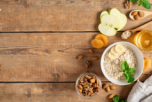 Ingredients for cooking healthy breakfast. Oatmeal, dried and fresh fruits, honey and nuts on a wooden table with copy space top view. Breakfast table concept - Valokuva, kuva