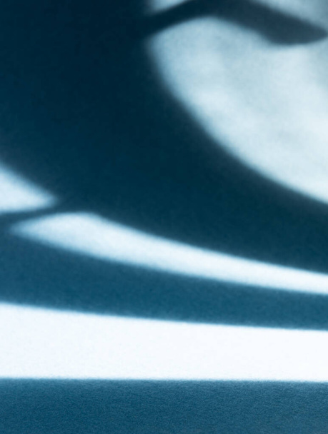 Absztrakt ívelt kemény árnyékok természetes fény által hajlított sötétkék haditengerészeti papír háttér. Szelektív fókusz. Természetes fény. Nagy másolási hely. Függőleges irány. - Fotó, kép