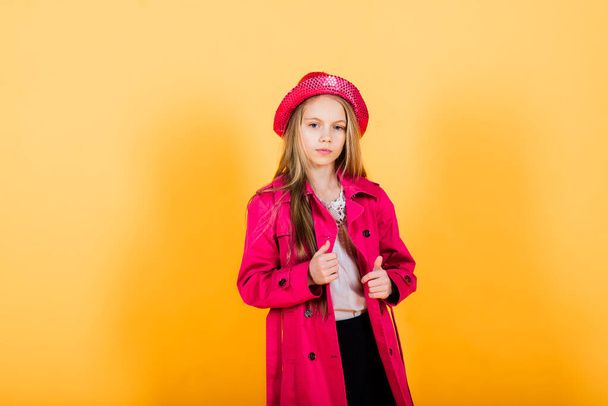 Portrait of happy girl in a raincoat and boots standing on yellow background - Photo, Image