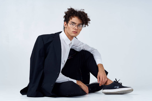 stylish man with curly hair in sneakers on a light background a jacket on the shoulder pants model - Photo, image