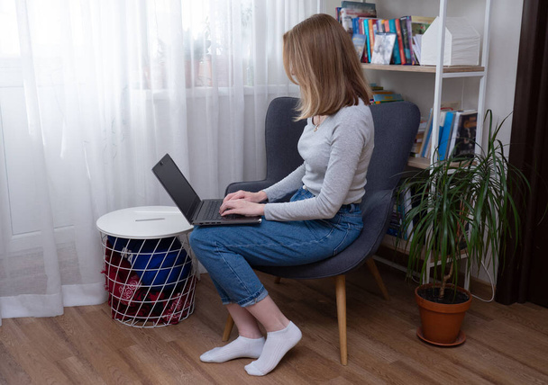 Woman using notebook while sitting in cosy armchair and working from home. remote work from home during quarantine and hard lockdown - Foto, Bild