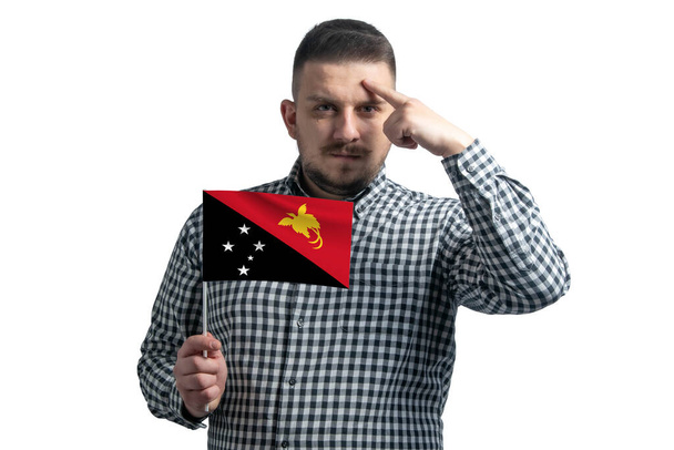 White guy holding a flag of Papua New Guinea and a finger touches the temple on the head isolated on a white background. - Photo, Image