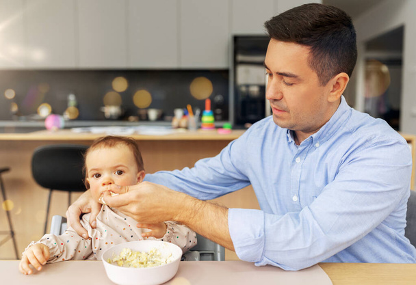 middle-aged father feeding baby daughter at home - Foto, afbeelding