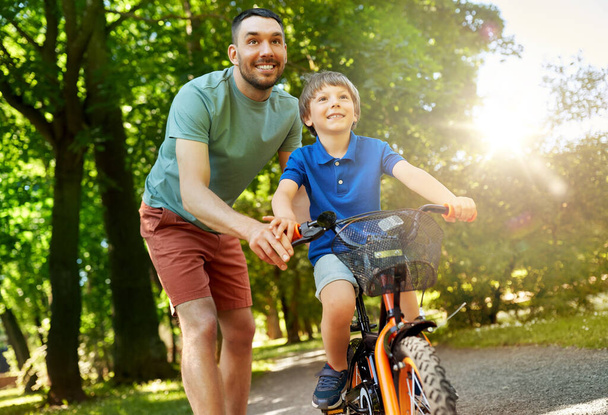 father teaching little son to ride bicycle at park - Foto, afbeelding