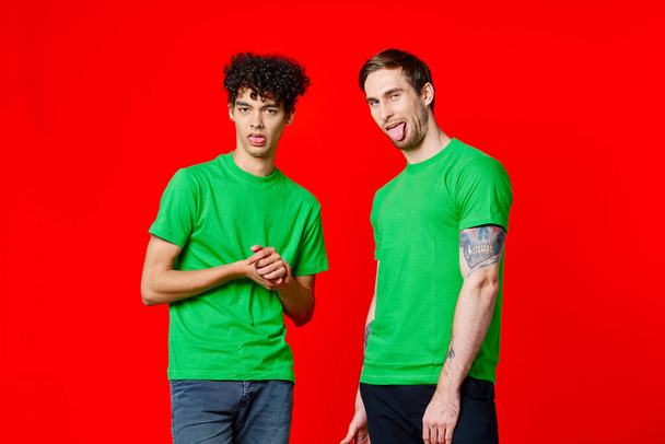 dva přátelé v zelených tričkách stojí vedle cínu s emocemi svých rukou - Fotografie, Obrázek