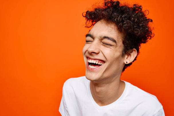 jeune homme en t-shirt blanc cheveux bouclés sourire fond orange - Photo, image