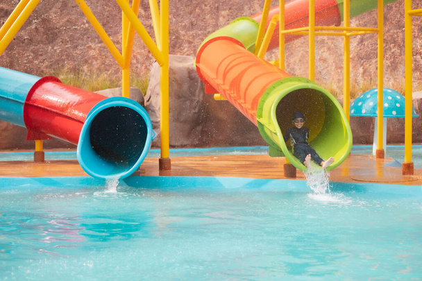 Asian child girl having fun to slide down on water slide in a water park at the summer time. - Photo, Image