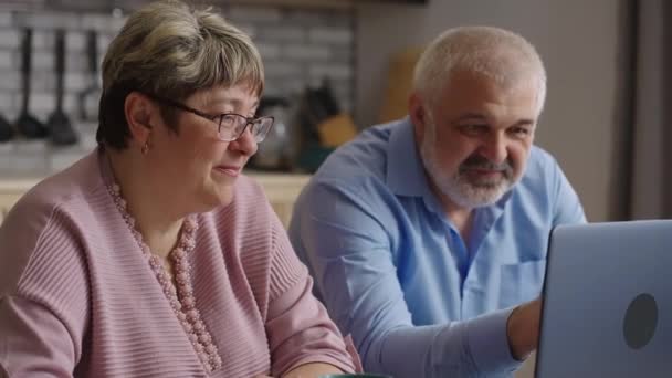 Rentner lernen den Umgang mit Laptop, surfen im Internet mit modernen Notebooks in der heimischen Küche, lächelnde ältere Ehepartner blicken auf den Bildschirm - Filmmaterial, Video