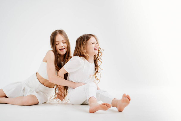 two little girls with long hair in white clothes. love between sisters.  - Фото, изображение