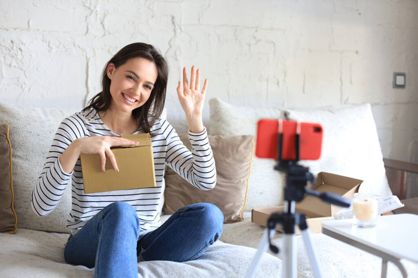 Young beautiful female blogger recording video while unpacking parcel at home - Foto, Imagem