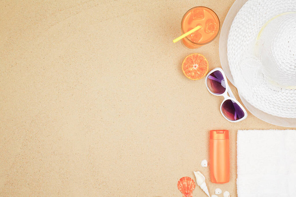 concept de fond de plage avec lunettes de soleil, jus d'orange, crème solaire et chapeau de plage sur sable
. - Photo, image